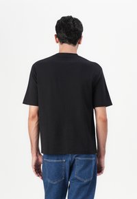 Black short-sleeve t-shirt with a classic crew neck. Made of smooth cotton material, featuring a relaxed fit and unadorned back design.