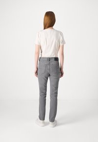Pelēkas pieguļošas džinses ar vienkāršu dizainu, divām aizmugurējām kabatām un melnu birku jostasvietā, apvienotas ar baltu īso piedurknju topu.