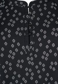 Tessuto nero con un motivo floreale bianco, dotato di una patta a bottoni con bottoni neri. La texture appare liscia con una leggera lucentezza.