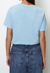 Sky blue cotton t-shirt with a round neckline, short sleeves, and smooth texture. Paired with high-waisted dark blue denim jeans featuring rear pockets.