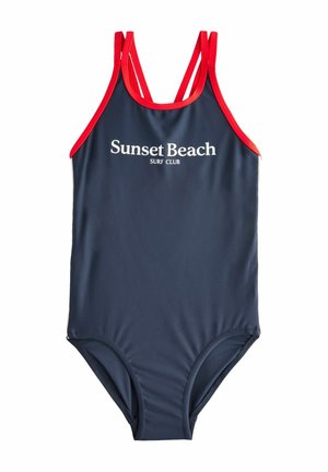 Maillot de bain une pièce bleu marine avec des accents rouges et des fines bretelles. "Sunset Beach SURF CLUB" imprimé en blanc sur le devant. Texture lisse.