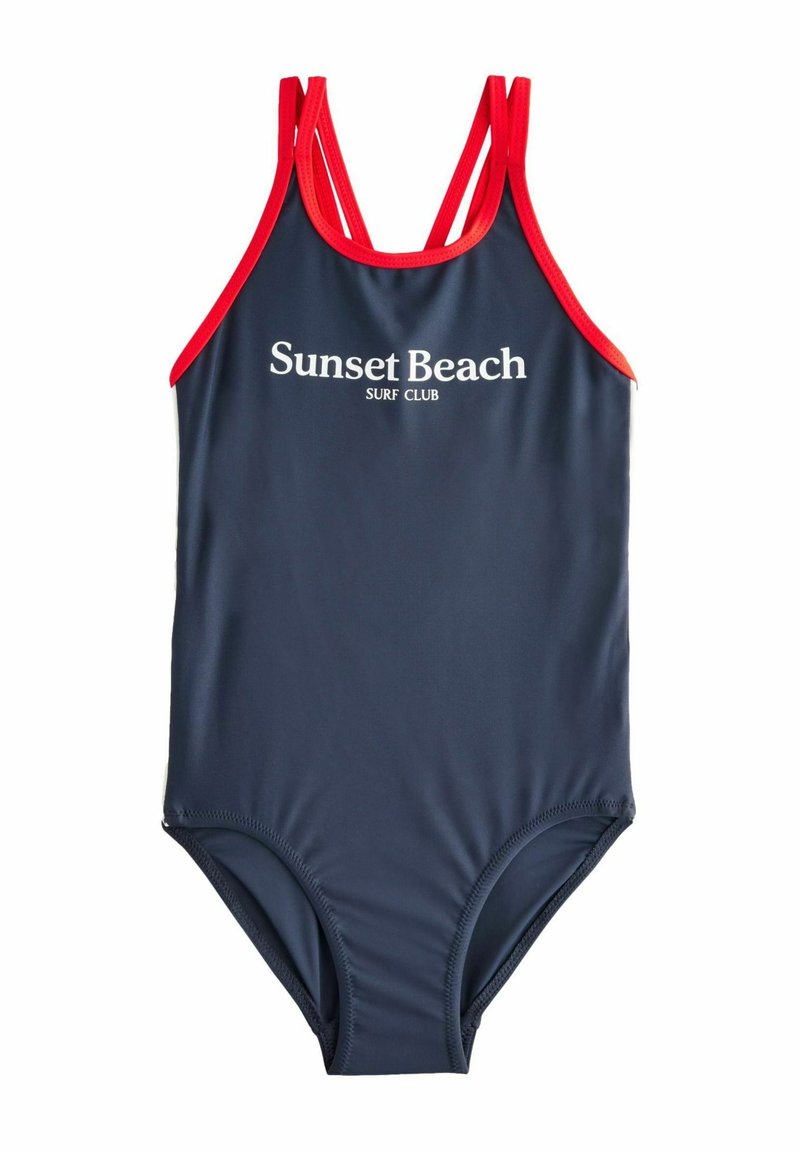 Bañador de una pieza en color navy con acentos rojos y tirantes finos. "Sunset Beach SURF CLUB" impreso en blanco en la parte frontal. Textura suave.