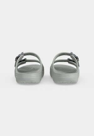Een paar grijze slip-on sandalen met dubbele verstelbare bandjes en gestructureerde voetbedden, gezien van achteren tegen een witte achtergrond.