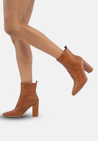 Botas de tobillo de tacón marrón con un patrón texturizado y tejido, punta afilada y cierre de cremallera en el lateral. Tacón grueso.