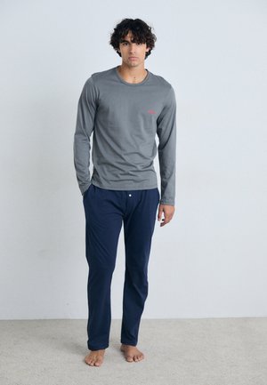 Chemise grise à manches longues avec un petit logo rouge, assortie à un pantalon bleu marine. Texture douce, coupe ajustée et design minimaliste.