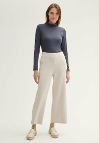Un pull col roulé bleu marine à manches longues, associé à un pantalon large crème avec des coutures verticales et des mocassins épais beiges.