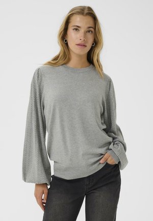 Pull en laine gris avec des manches ballon texturées en tricot à torsades, un col rond et un tissu doux. Associé à un jean foncé, mettant en avant une coupe décontractée.