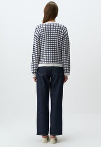 Wit gebreid sweater met een marineblauw ruitpatroon, ronde hals en geribbelde manchetten. Gecombineerd met een paar wijde donkerdenim jeans en lichte schoenen.