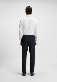 White long-sleeve shirt with a pointed collar, paired with dark navy trousers featuring an elastic waistband and side pockets.