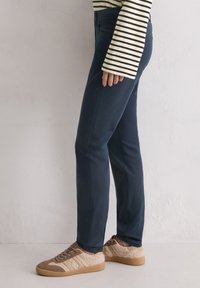 Marineblauwe broek met een gladde textuur, slim fit en zakken, gecombineerd met bruine sneakers van een mix van suede en stof.