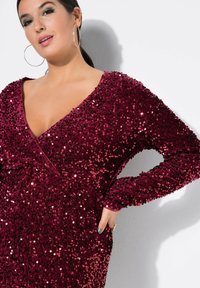 Burgundská šaty s flitry a hlubokým výstřihem do V, dlouhými rukávy. Hladká texturou a přiléhavý střih s kapsami, odrážející světlo od flitrů.