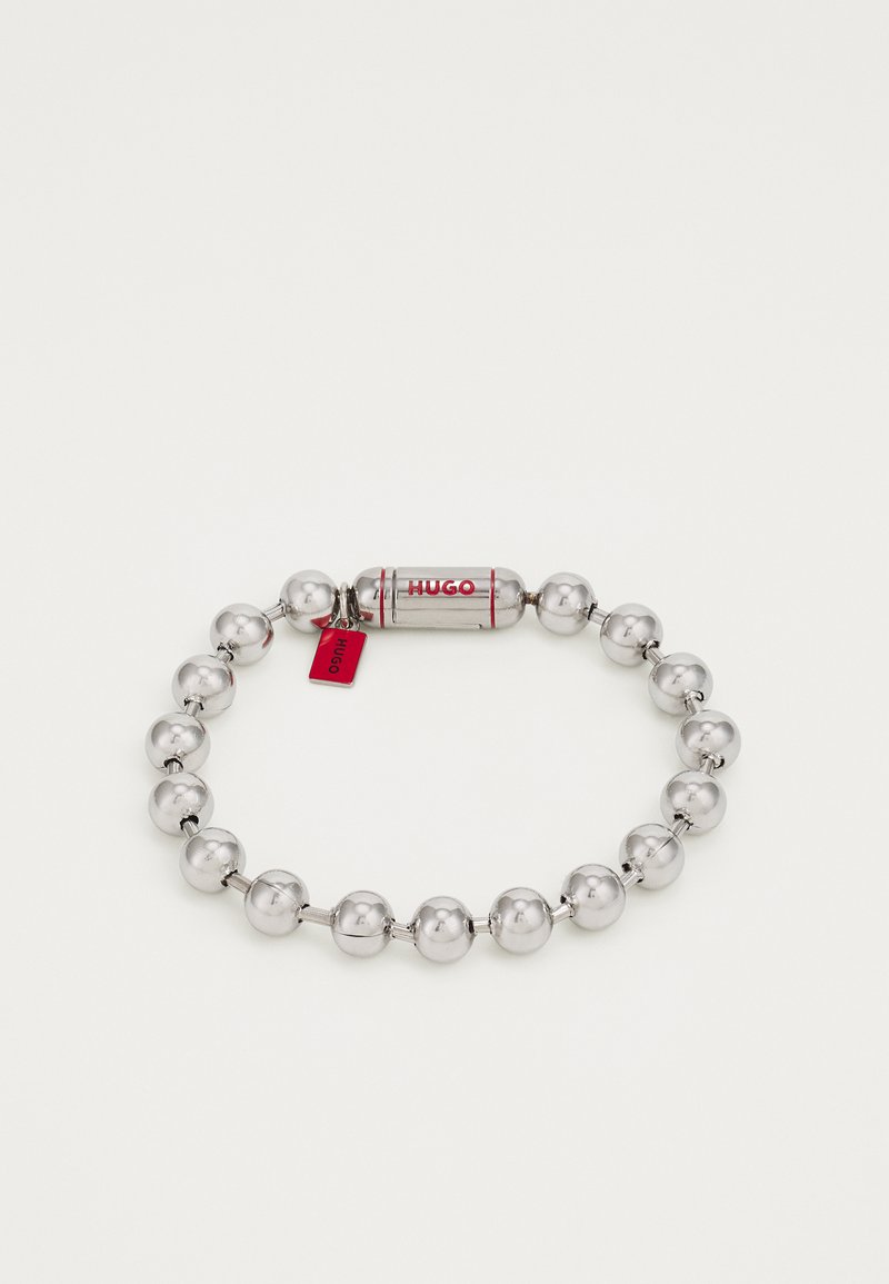 Bracciale in argento con perle metalliche rotonde, caratterizzato da una capsula centrale con il testo "HUGO" in rosso e un piccolo tag rosso attaccato.