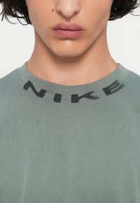 Zelo blizu osebe, ki nosi zeleni majic s črnimi črkami, ki obkrožajo ovratnik in pravijo "NIKE".