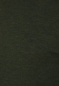 Ciemnozielona dzianinowa koszulka o miękkiej fakturze. Posiada małe haftowane logo "CK" w ciemnym kolorze na dolnej części.