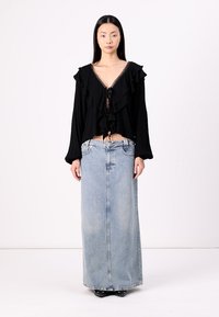 Svart blus med volanger och långa ärmar, med en knytning fram och djup ringning, kombinerad med en högmidjad, ljusblå denim-maxikjol.