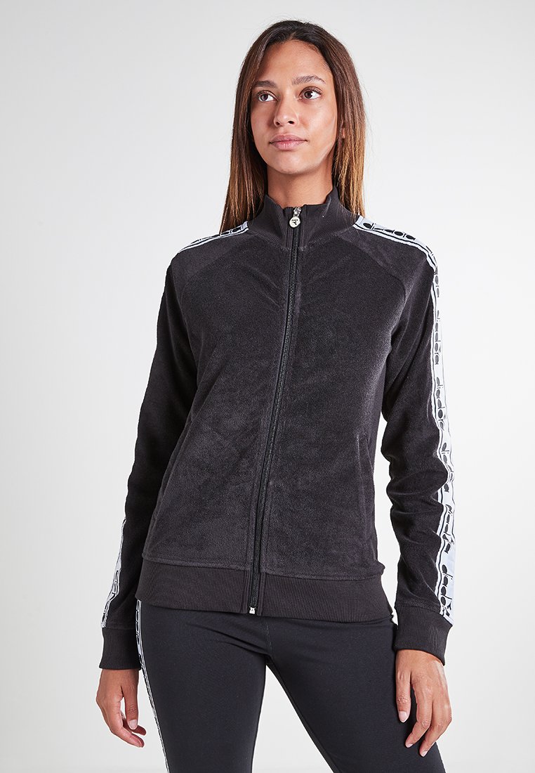Giacca in pile nera con zip e colletto alto, caratterizzata da strisce laterali bianche e polsini a coste. Tessuto morbido, design aderente.