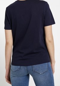 Námorně modré bavlněné tričko s kulatým výstřihem a krátkými rukávy. Zadní strana je hladká s uvolněným střihem. Materiál je hladký a mírně elastický.