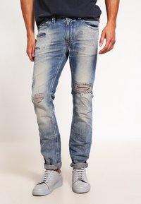 Huvudblå denimjeans med tapered passform, prydda med flera revor och blekta partier, fulländade med en uppvikt fåll och standardfickor.