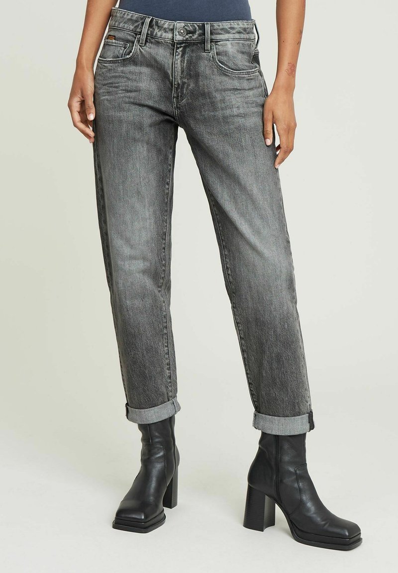Grå denimjeans med en falmet finish, tapered passform, oppbrettede hemmer og to frontlommer, sammen med svarte chunky-helte ankelstøvler.