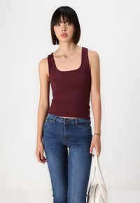 Débardeur ajusté bourgogne avec décolleté carré, associé à un jean skinny bleu. Le haut a une texture lisse et un minimalisme dans ses détails.