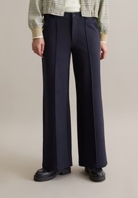 Navy wijde broekspijpen gemaakt van zachte stof, met voorplooien en een vlakke voorkant. Gecombineerd met dikke zwarte plateauzolen.