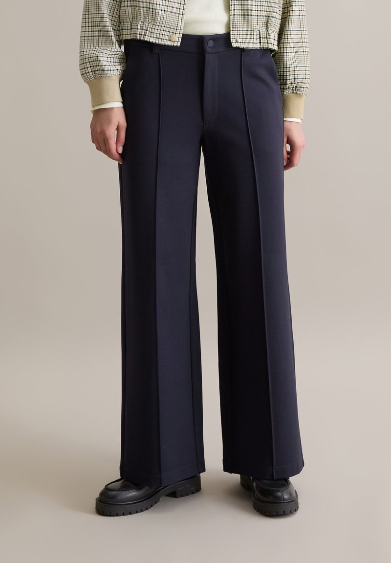 Navy wijde broekspijpen gemaakt van zachte stof, met voorplooien en een vlakke voorkant. Gecombineerd met dikke zwarte plateauzolen.