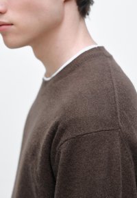 Brun stickad tröja med rund halsringning, med en slät struktur och avslappnad passform. Tyget verkar mjukt och mysigt.