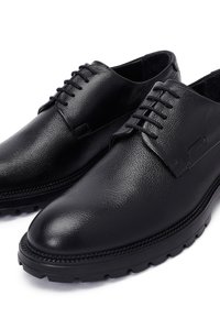 Zwarte leren schoenen met een gladde textuur, ronde neus, verhoogde veters en een dikke rubberen zool met antislipprofielen.