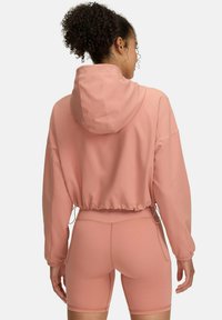Šviesiai rožinė trumpa hoodie su reguliuojama gobtuvu ir elastingu apvadu. Turi ilgas rankoves ir lygaus, tamprumo audinio, derinama su atitinkamomis šortais.