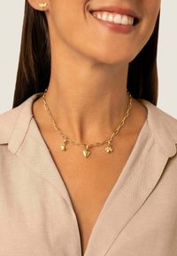 Collana in oro con tre ciondoli: una stella, un cuore e un'impronta di zampa, indossata su un top beige chiaro con colletto.