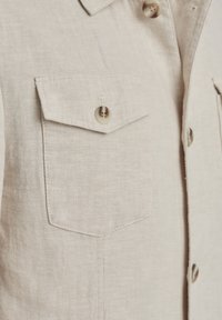 Beige Hemd mit Knopfleiste und Fischgrätenmuster, ausgestattet mit zwei Brusttaschen und hellbraunen Knöpfen. Klassisches Kragendesign.