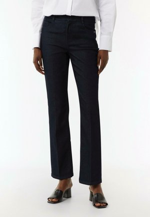 Dunkelblaue Denim-Jeans mit geradem Schnitt, Fünf-Taschen-Design und dezenten Nähten. Kombiniert mit schwarzen, hohen Mules.