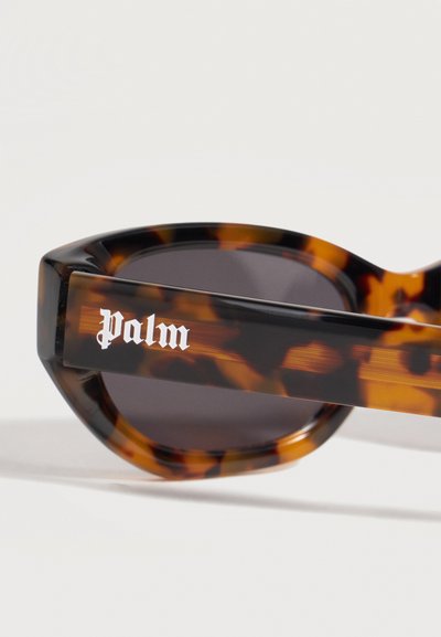 Lunettes de soleil à motif écaille avec verres foncés, portant le nom de la marque "Palm" en police gothique blanche sur la branche.