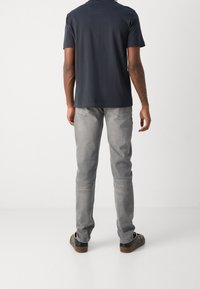 Marinblå kortärmad t-shirt, grå slim-fit-jeans och svarta sneakers. Jeansen har en urtvättad textur och bakfickor med diskret sömnad.