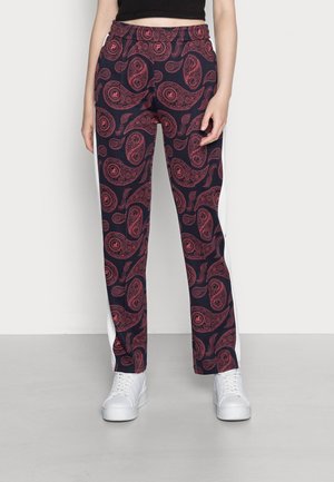 Person iført marineblå bukser med røde paisley-mønstre og hvide striber på siderne, stylet med hvide sneakers og en sort cropped top.