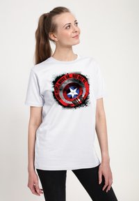 Hvid bomulds t-shirt med et cirkulært grafik med røde og sorte accenter, en blå stjerne og teksten "Nogle mennesker kommer videre... men ikke os."