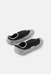 Svarta och grå filtsandaler med rundad form, beige elastisk kant och en liten etikett på sidan. Mjuk textur, minimalistisk design.
