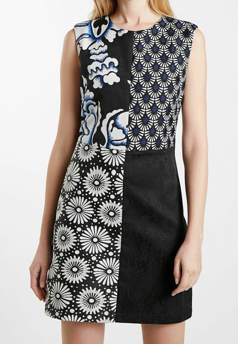 Robe sans manches avec quatre panneaux à motifs noirs et blancs comprenant des dessins floraux, abstraits et en éventail, portée par une personne debout.
