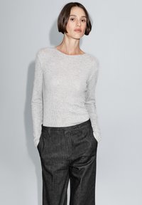 Light grey long-sleeve top made of textured fabric, paired with dark grey, loose-fitting trousers. Both garments feature a simple design.