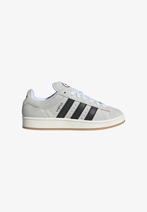 Grå ruskinds sneakers med hvide snørebånd og en hvid sål. Har tre sorte striber og et rundt logo på tungen. Gummisål i gummi.