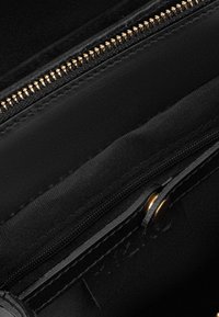 Black leather bag interior featuring a smooth texture, gold zipper detail, and a sleek design with multiple pockets for organization.