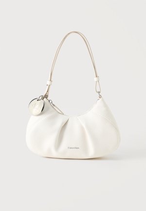 Weiße strukturierte Calvin Klein Schultertasche mit kurzem Riemen und rundem silbernem Logoanhänger in der Nähe des Reißverschlusses.