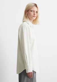 Lightly striped button-up shirt in pale beige, featuring a pointed collar, long sleeves with buttoned cuffs, and a relaxed fit.
