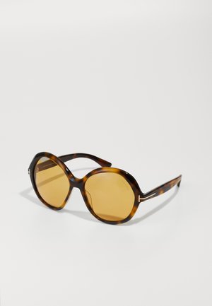 Lunettes de soleil en écaille de tortue avec de grandes lentilles ovales, lentilles ambrées, et branches fines dotées d'un accent argenté pour une touche moderne.