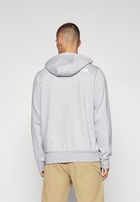 Sudadera gris con capucha ajustable, puños y dobladillo acanalados. Presenta un pequeño logo blanco en el hombro. Fabricada con un tejido suave.