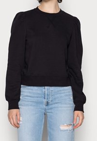 Svart bomullströja med puffärmar och ribbad fåll. Har en rund halsringning och en mjuk textur. Kombineras med ljusblå jeans.