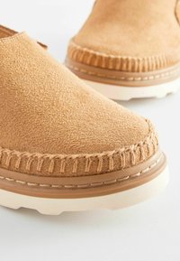 Svijetlosmeđi slip-on cipele od mekog antilopa s šavovima na rubu i teksturiranom gumenom potplatu, s dizajnom zaobljenog vrha.