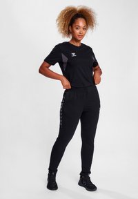Sort atletisk outfit bestående af en t-shirt med grå paneldetaljer og matchende joggingbukser med sidelister. Letvægts, tætsiddende design.