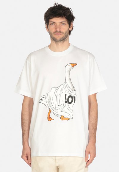 Uomo che indossa una maglietta bianca oversize con un'anatra a cartoni animati sul davanti, l'anatra indossa una maglietta con la scritta "AMORE".