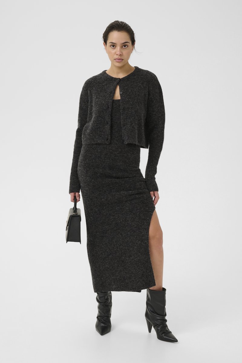 Sort strikket cardigan kombineret med en matchende lang kjole med en sideslids. Båret med sorte hæle støvler og holder en lille håndtaske.